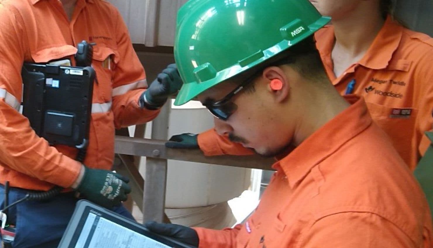 Man in orange high visibility gear and personal protective equipment with a digital tablet, doing work on the SMARTapps application.